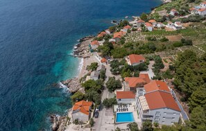 An aerial view of a coastal residential area with houses, a swimming pool, and a rocky shoreline. - Awesome apartment in Dingac with lake view (Dingac)