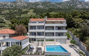 Um edifício com vários andares, piscina, varandas e vista para uma paisagem montanhosa.