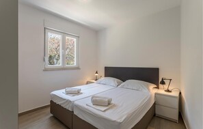 Quarto com duas camas, uma janela, mesas de cabeceira com luminárias e piso de madeira.