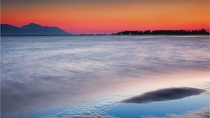 A calm body of water reflecting a sunset with mountains in the background.
