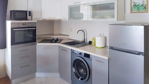A compact kitchen with a microwave, oven, sink, washing machine, and refrigerator.