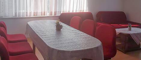 A conference room with a long table, red chairs, a small table with a vase, and a window with sheer curtains.