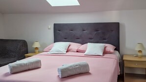 Una cama bien hecha con ropa de cama rosa y almohadas blancas, dos mesitas de noche con lámparas, y una butaca tapizada oscura.