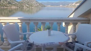 Un balcón con una mesa y dos sillas, con vista a un lago tranquilo y montañas.