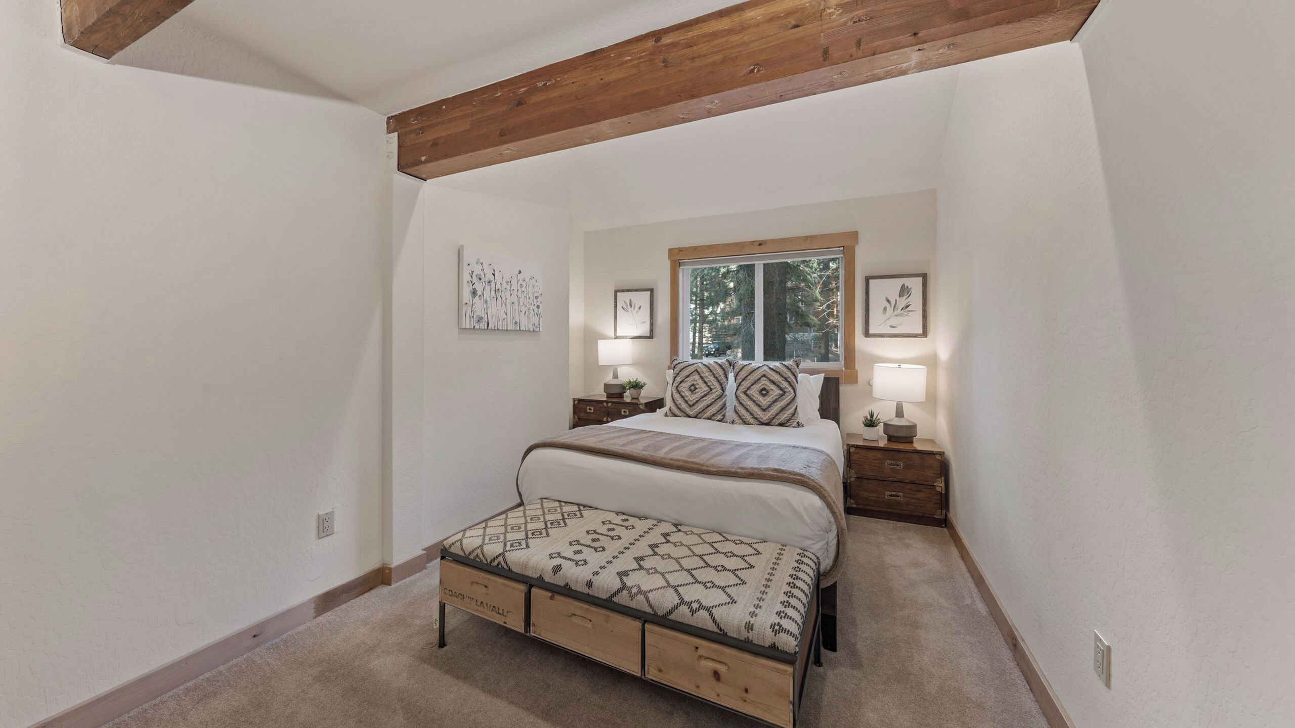 A bedroom with a bed, nightstands, a window, and a view of trees.