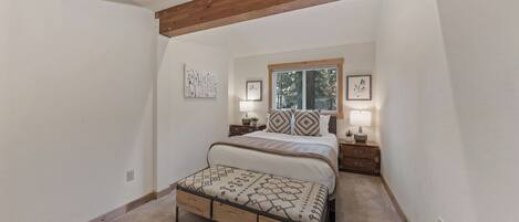 A bedroom with a bed, nightstands, a window, and a view of trees.
