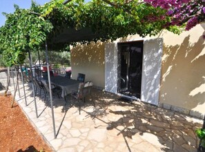 Eine Terrasse im Freien mit Steinboden, einem Tisch mit Stühlen und einer mit Grünpflanzen bewachsenen Pergola.