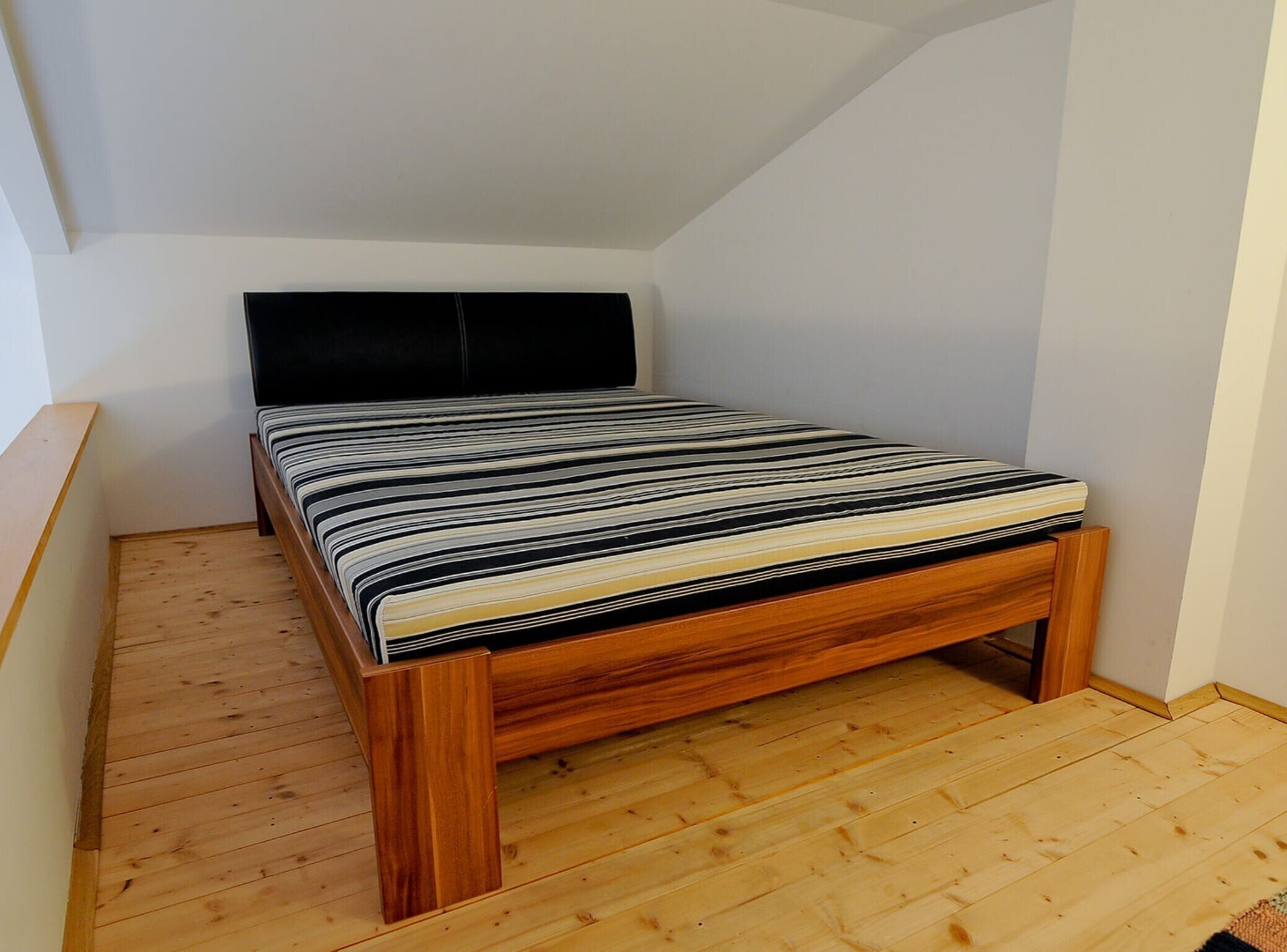 A small, wooden-framed bed with a black headboard in a room with white walls and wooden flooring.