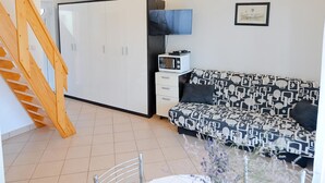 A compact living space with a sofa, a microwave, a TV, and a staircase. - Apartments Jurić - One Bedroom Apartment With Terrace (Plavi) (Kali)