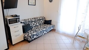 A compact living space with a sofa, a television mounted on the wall, a microwave, and a small table with a chair. - Apartments Jurić - One Bedroom Apartment With Terrace (Plavi) (Kali)