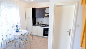 A compact kitchen with white cabinets, a stove, and a sink. There is a dining table with chairs and a vase with flowers. - Apartments Jurić - One Bedroom Apartment With Terrace (Plavi) (Kali)