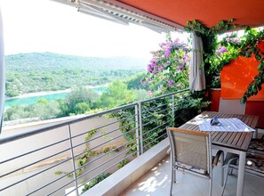 Ein Balkon mit Blick auf einen Fluss und Hügel, ein Tisch mit Stühlen und einer Zierpflanze.