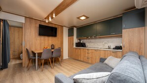Una cocina compacta con armarios de madera, un comedor con mesa y sillas, y un sofá gris con un cojín.