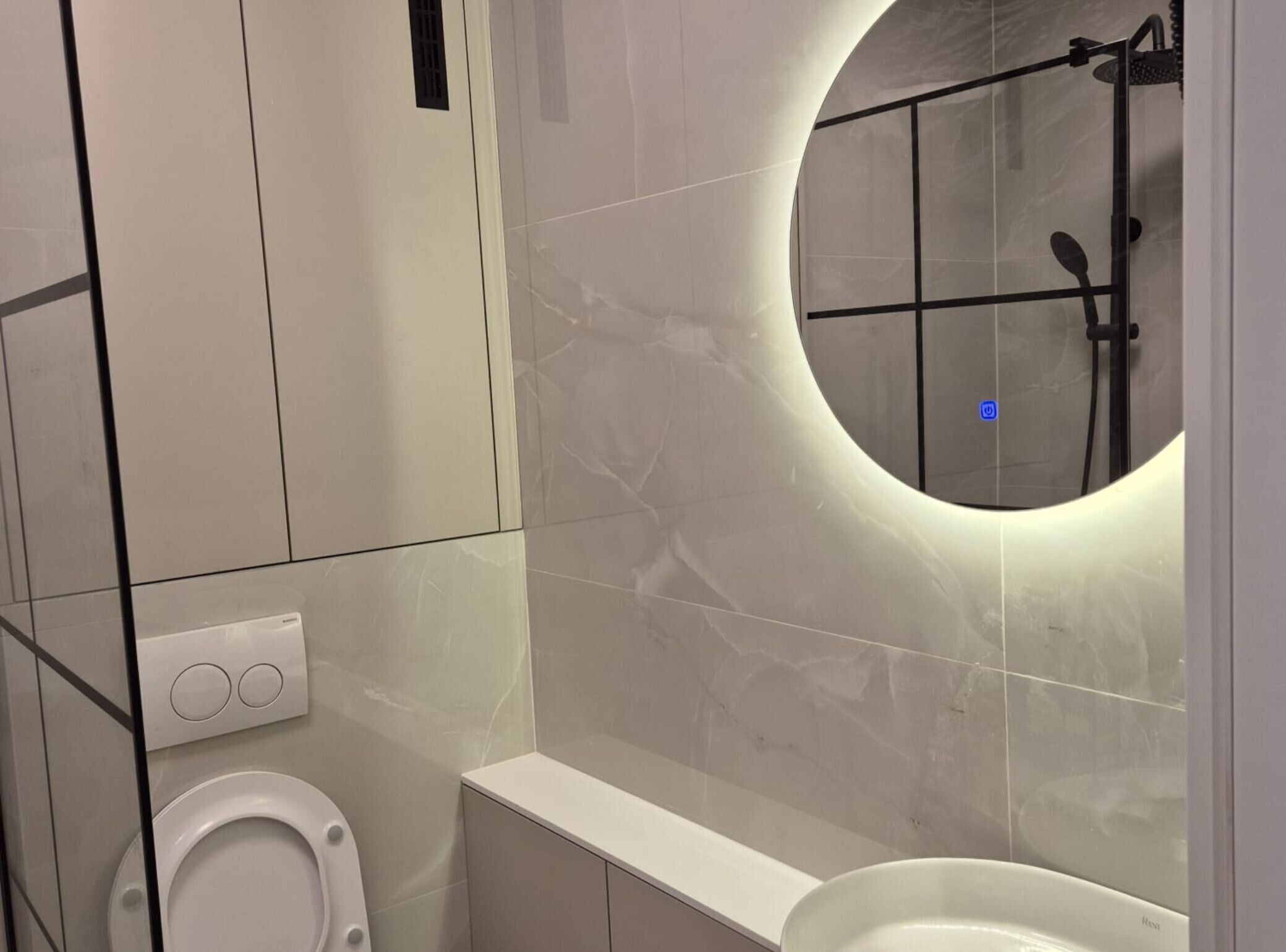 Une salle de bain moderne équipée de toilettes, d’un lavabo et d’une douche, avec un miroir rond.