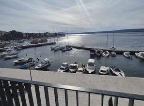 En småbåtshamn med olika typer av båtar förtöjda, en klar himmel och ett avlägset utsiktsläge med kullar i horisonten.