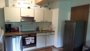 Una cocina con armarios blancos, lavavajillas de acero inoxidable, horno empotrado, cafetera y refrigerador.