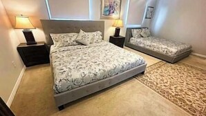 A bedroom with a large bed, a smaller bed, two bedside tables, and a patterned rug. - Luxury 4BR Home Near Square One, with King Bed (Mississauga)