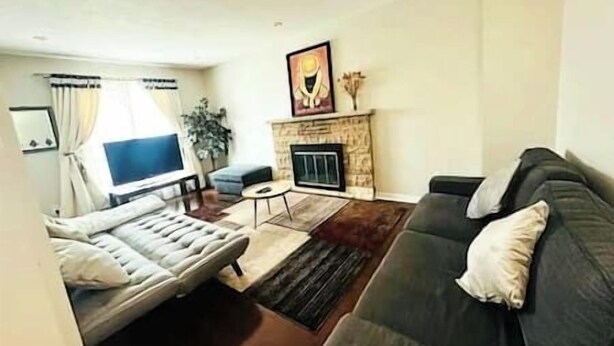 A living room with a sofa, a television, a fireplace, and a painting on the wall. - Luxury 4BR Home Near Square One, with King Bed (Mississauga)