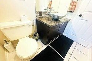 Un baño con inodoro, lavamanos y un tapete negro en el suelo.