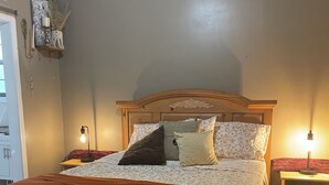 A bedroom with a wooden bed, two bedside tables, a nightstand, and a hanging light fixture.