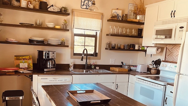 A kitchen with a wooden island, white cabinets, a window, and various kitchen appliances.