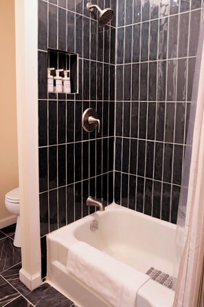 Une salle de bain avec un mur de douche recouvert de carreaux noirs, une baignoire blanche et des toilettes.