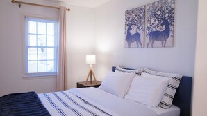 A bedroom with a bed, a window with curtains, a bedside lamp, and two wall art pieces depicting deer. - Quiet & Modern. Close to WFU-Reynolda. Patio Fenced. (Winston-Salem)