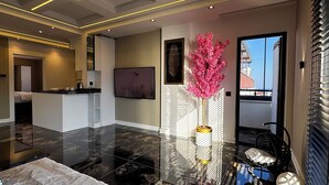 Un moderno vestíbulo de hotel con piso de baldosas negras, un arreglo floral rosa en el centro, un área de descanso con sillas blancas acolchadas y un televisor montado en la pared.