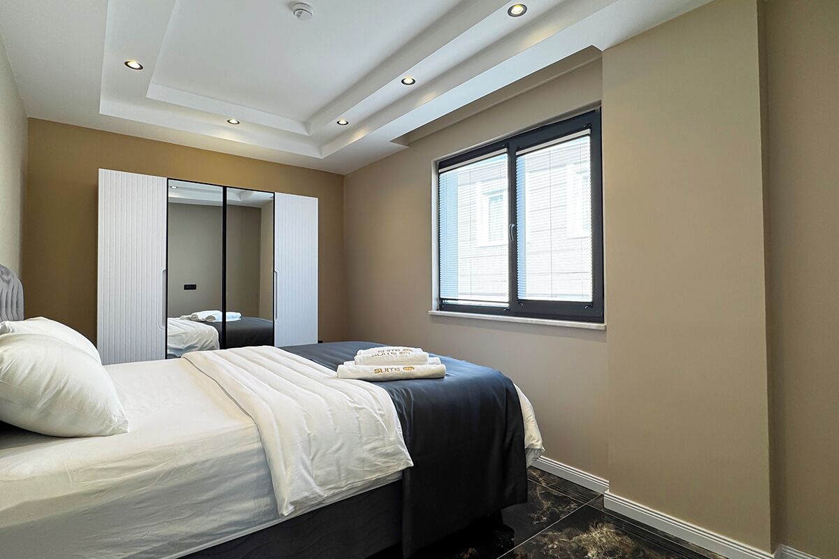 Una habitación de hotel con una cama, un espejo grande, una ventana con persianas y un techo con iluminación empotrada.