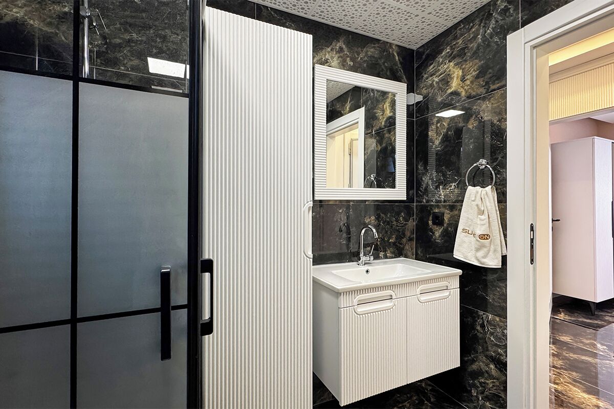 A modern bathroom with a white vanity, a large mirror, and a black marble wall.