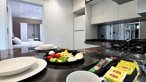 Una cocina moderna con encimera de mármol, zona de comedor con platos blancos y diversos alimentos, y un minibár visible.