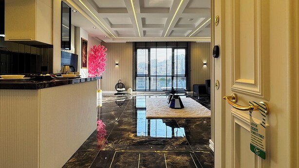 Un moderno vestíbulo de hotel con piso de mármol, una recepción, un ventanal con persianas y una escultura decorativa rosa.