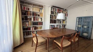 A dining area with a wooden table, wicker chairs, and bookshelves filled with books. - WITHIN WALKING DISTANCE, SAINT GERMAIN AS LES INVALIDES, THE RODIN MUSEUM, (Paris)