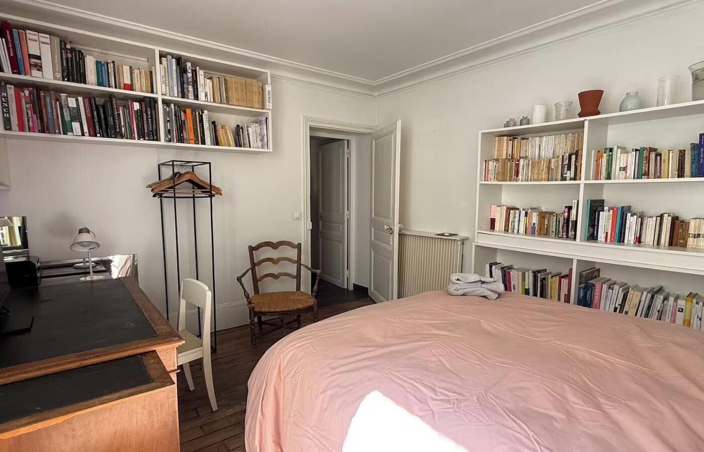 A bedroom with a bed, a desk, a chair, a bookshelf, and a radiator.