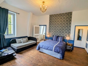 A bedroom with a bed, a sofa, a small table, a chandelier, and patterned wallpaper. - La Chambre Royale - Domaine de la Dordrona (Bourdeilles)