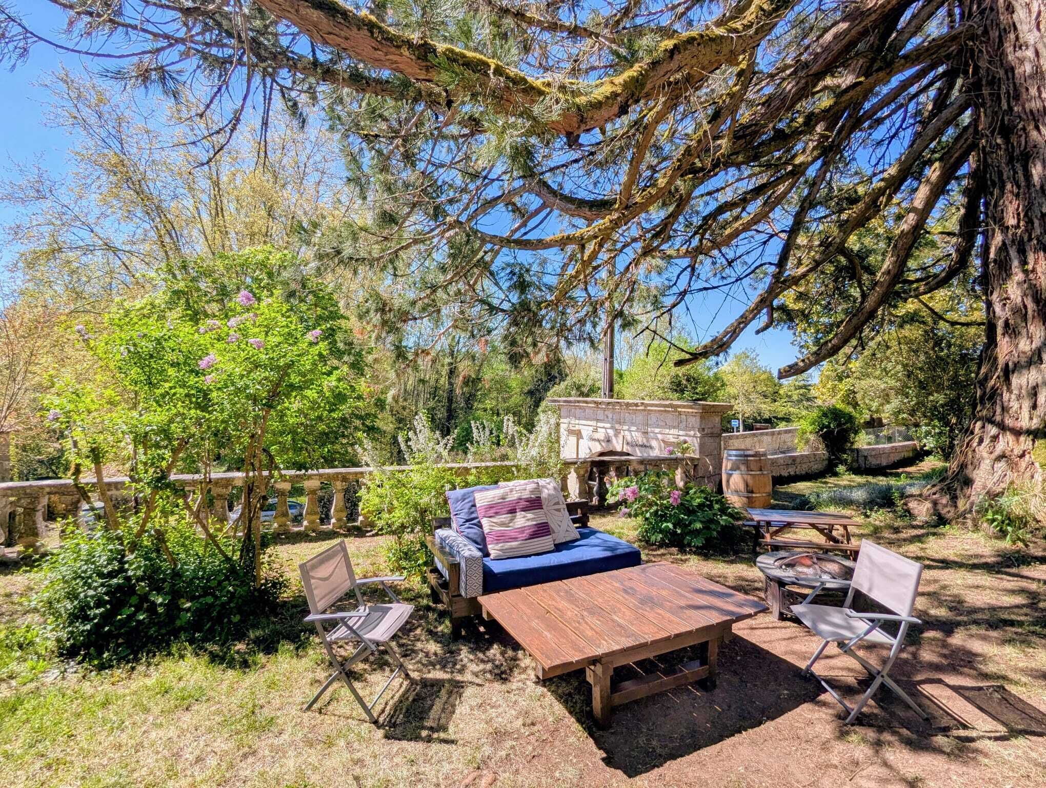 Un espace extérieur aménagé avec un banc en pierre, une table en bois et deux chaises pliantes.