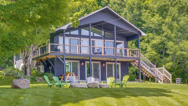 A two-story house with a balcony, outdoor seating, and a staircase leading to the upper level. - Seymour Lake Across St! Scenic Home w/ Hot Tub (Morgan)