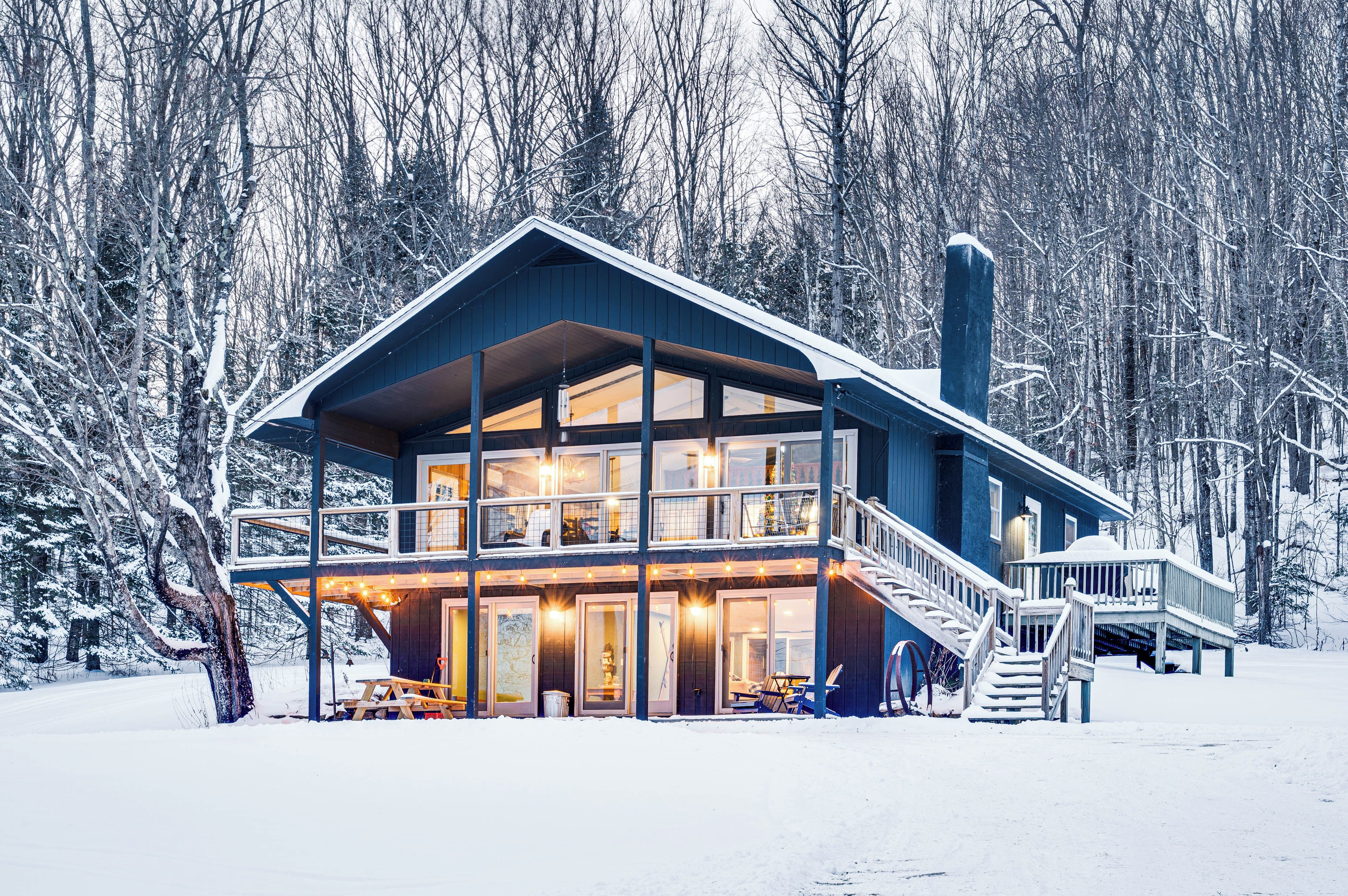 A two-story lodge with a balcony and a staircase, surrounded by snow-covered trees.