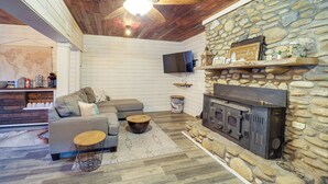 Un salon chaleureux avec une cheminée en pierre, un ventilateur de plafond et un téléviseur fixé au mur.