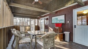 A covered outdoor area with wicker furniture, a glass table, and a door with a view of a snowy landscape.