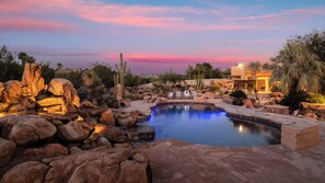 A landscaped pool area with rocks, a small waterfall, and a building in the background. - 5bdr Oasis w/ Waterfall Pool, Hot Tub, Desert View Desert Cascase by Avantstay (Carefree)