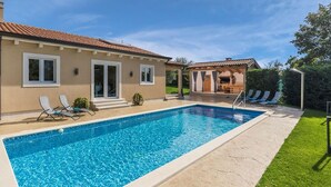 Una piscina amb gandules, un porxo cobert i una casa amb teulada de rajola.