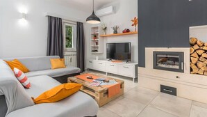Un saló modern amb un sofà gris, coixins taronja, una taula baixa de fusta, un televisor i una xemeneia.