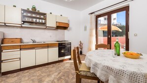A compact kitchen with a dining area, a table with a lace tablecloth, and a view of the outside through a window. - 2 bedroom lovely apartment in Pag (Pag)