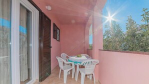 Un balcone con tavolo e sedie, una porta scorrevole in vetro e vista sul verde.
