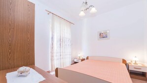 Una camera da letto con un'armadio in legno, un letto con copriletto rosa, due comodini con lampade, una finestra con tende trasparenti e un quadro appeso al muro.