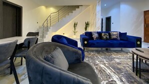 Ein modernes Wohnzimmer mit Treppe, einem blauen Sofa und einem Essbereich.