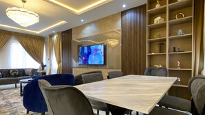 Uma sala de jantar moderna com uma mesa de mármore, cadeiras estofadas cinzentas e uma televisão de tela plana grande fixada na parede.