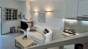 Un salon moderne avec un canapé blanc, une table basse, une cheminée et un coin cuisine doté de placards et d’un plan de travail.