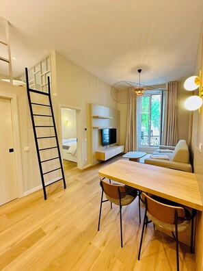 A modern living room with a wooden dining table, a sofa, a TV, and a balcony with curtains. - Architect designed apartment - Carré d'Or (Nice)
